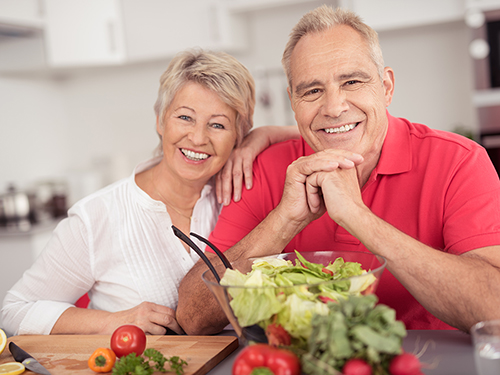 Active adult couple in kitchen cooking>